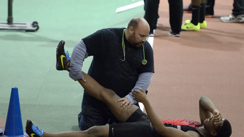 Athlete lying on a track while a medic stretches his cramping leg